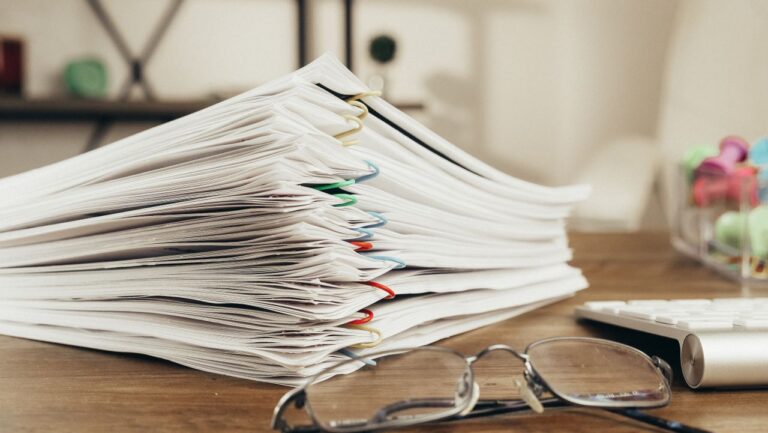 Close-up of a stack of office papers on a desk with glasses, emphasizing organization.
